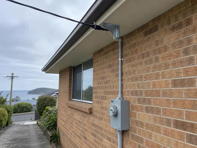 Overhead service cable and point-of-attachment bracket on a brick house exterior in Forresters Beach